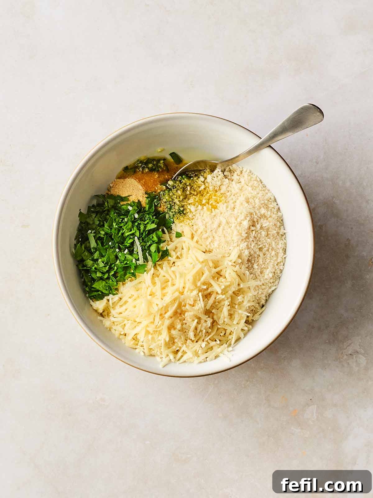 Herb Butter Chicken Pasta 7 A small bowl holding panko breadcrumbs, grated Parmesan cheese, garlic granules, and chopped parsley, with a spoon ready to mix the ingredients for the crispy topping.