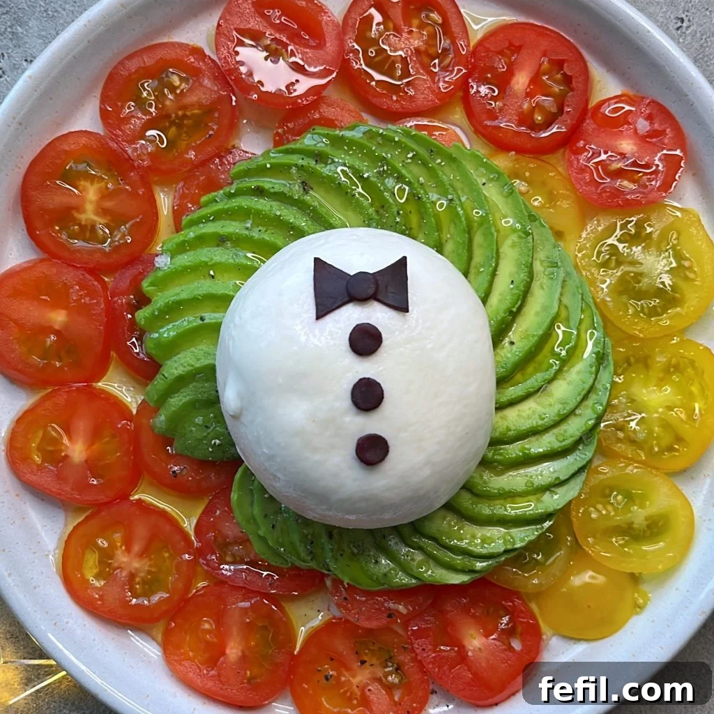 A meticulously arranged plate showcasing sliced red and yellow cherry tomatoes forming a colorful ring. At the center rests a creamy ball of burrata, elegantly topped with fanned-out avocado slices and a delicate red cabbage bow-tie, ready to be served.