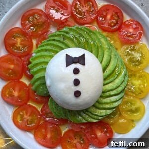 A vibrant Burrata Salad on a plate with fanned avocado slices and cherry tomatoes, crowned with a distinctive bow-tie detail.