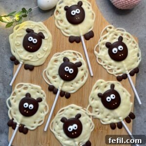 Seven sheep-shaped chocolate lollipops featuring soft white chocolate bodies and distinct dark chocolate faces, feet, and ears are neatly arranged on a rustic wooden board. These playful and adorable bites are ideal additions to festive food recipes or party dishes, each complete with large, captivating white candy eyes.