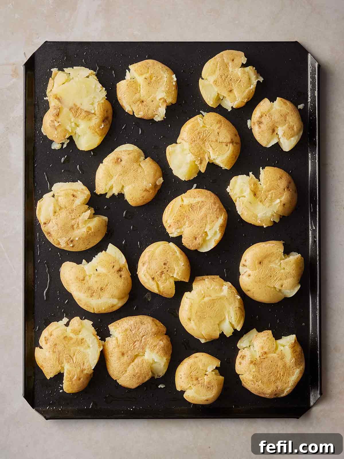 A baking tray filled with smashed potatoes, yet to be cooked.