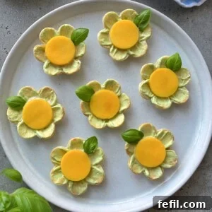A plate of seven flower-shaped crackers topped with avocado appetizer spread, a yellow circular slice in the center, and a basil leaf garnish, arranged neatly on a round white plate.