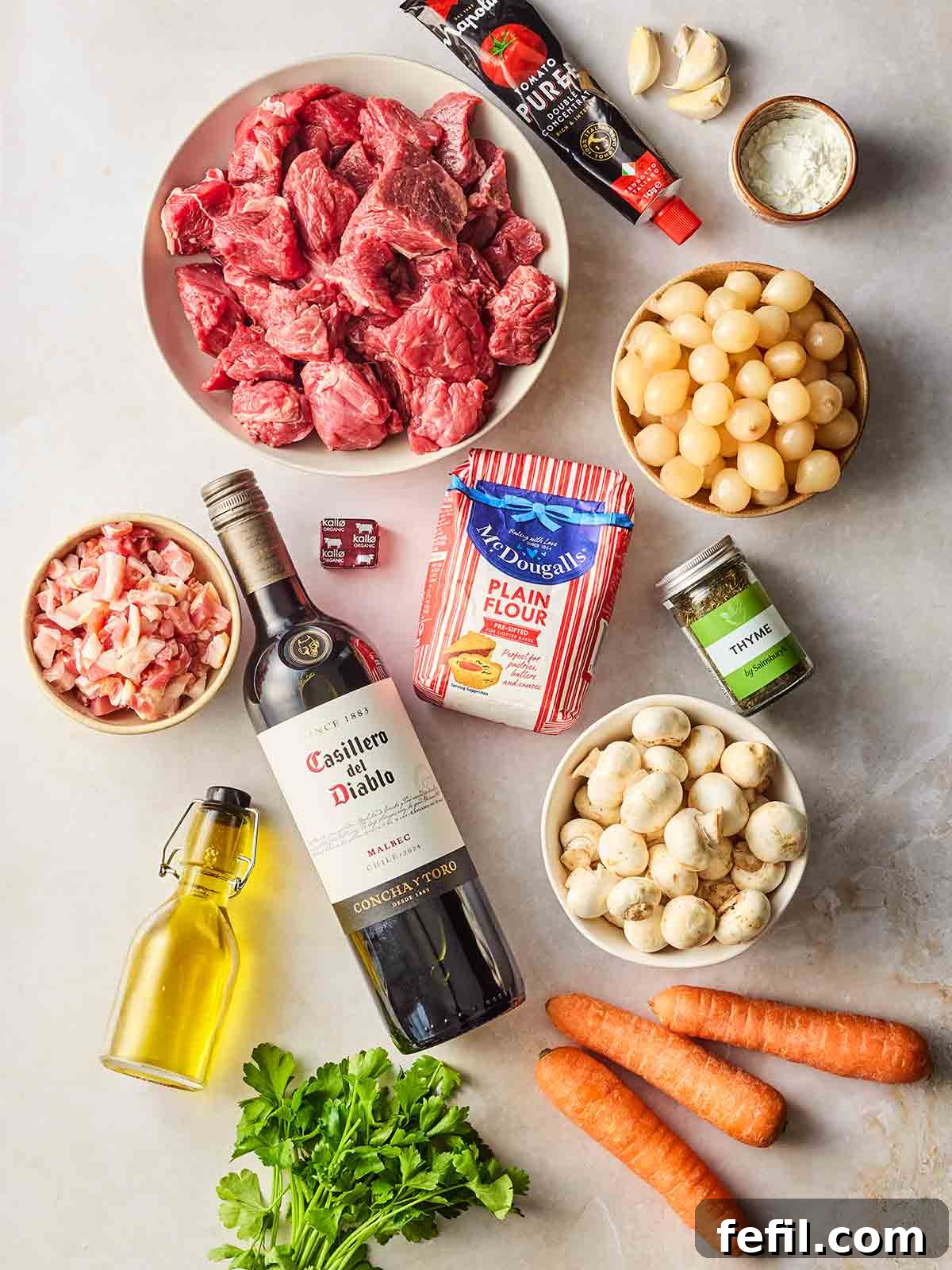 All the fresh ingredients for making beef bourguignon carefully laid out on a clean white surface, showcasing their quality and readiness for cooking.