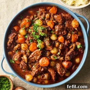 A large pot of homemade Beef Bourguignon, on a table, ready to serve with mashed potatoes.