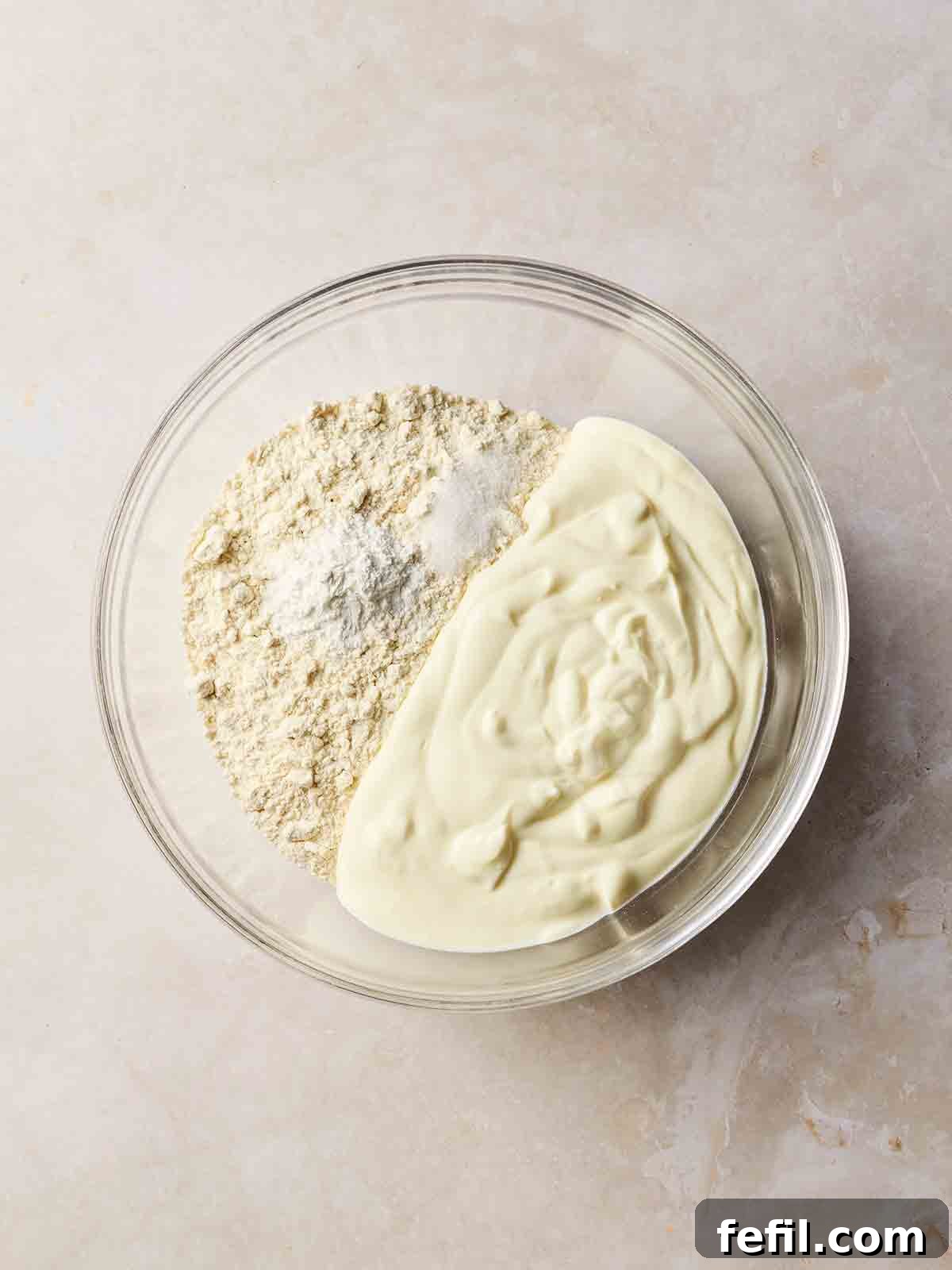 A bowl of natural yogurt, self-raising flour, baking powder, and salt, ready to be mixed together.