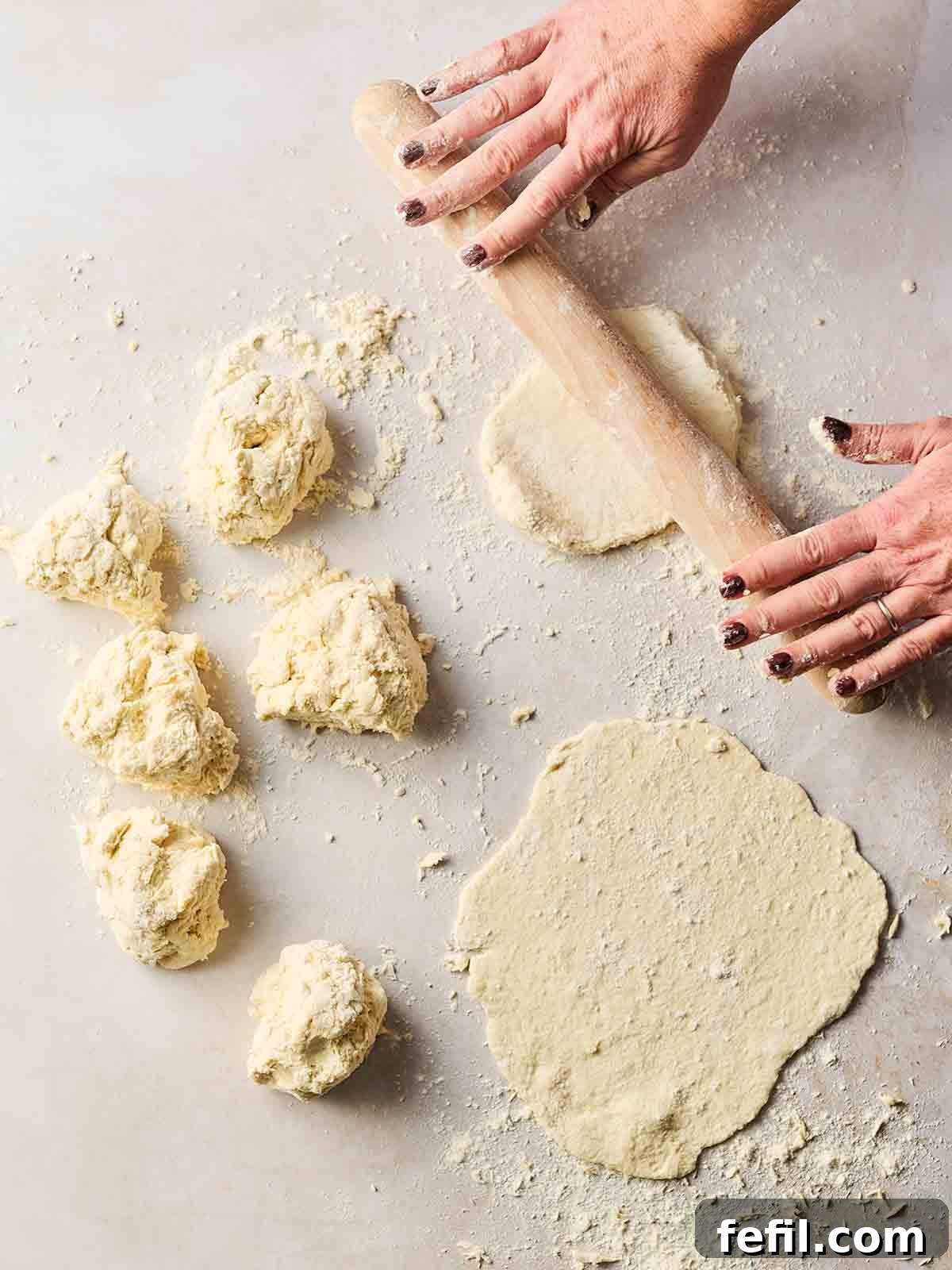 Portioned out flatbread dough on a white surface, being rolled out into a round shape with a rolling pin.
