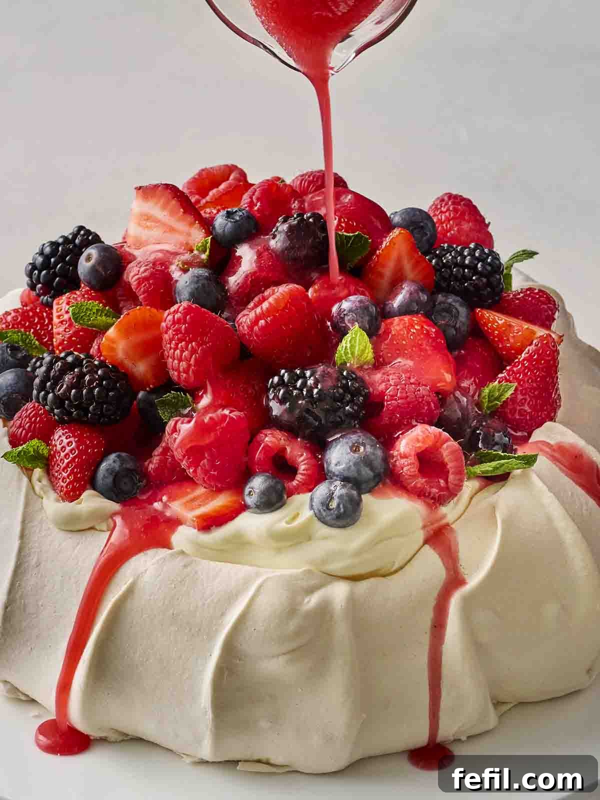Perfect Pavlova, Made Simple 2 A beautifully garnished Pavlova with fresh berries and a drizzle of vibrant red sauce, ready to be served.