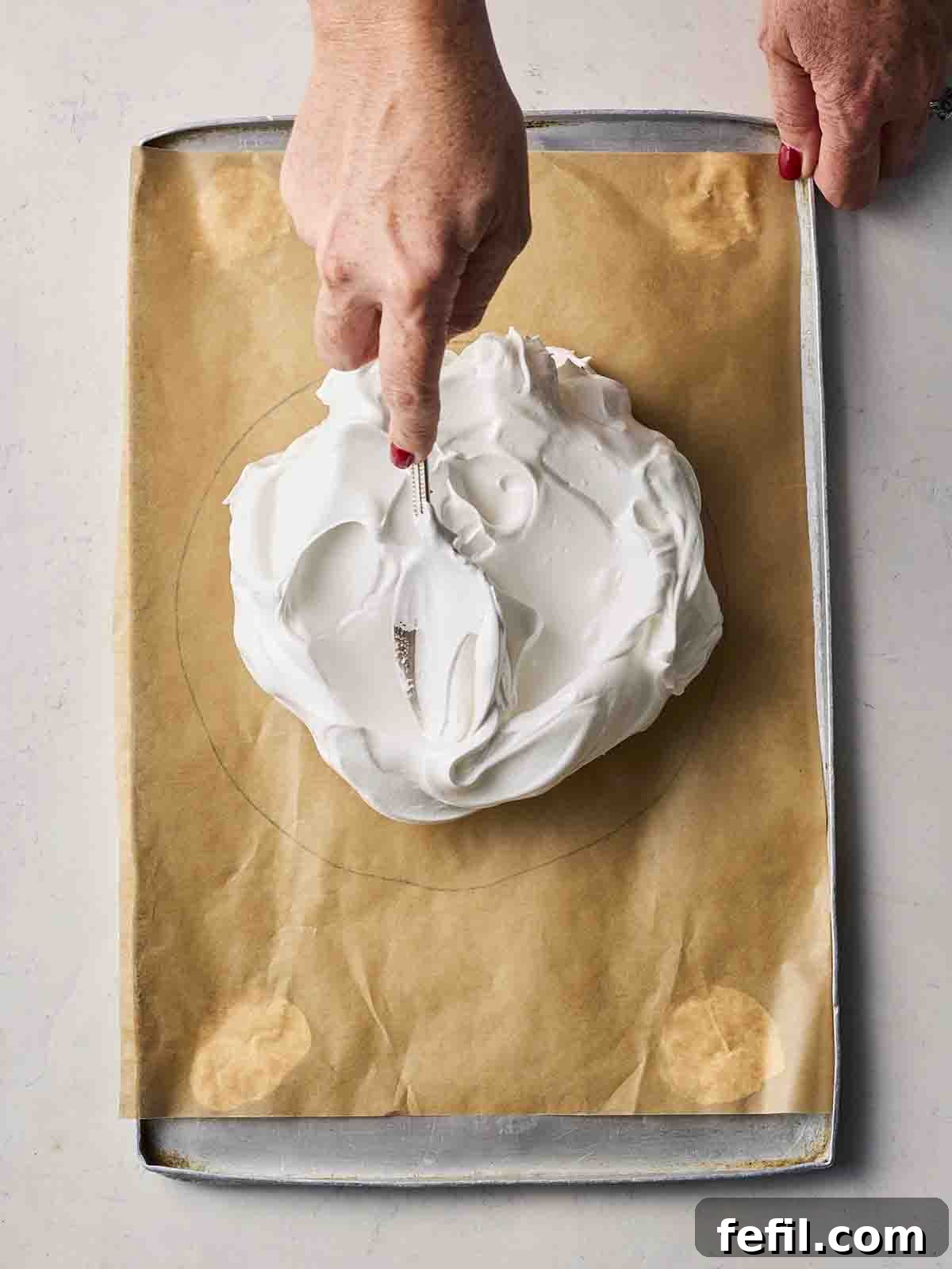 Perfect Pavlova, Made Simple 6 A hand carefully spreading meringue mixture onto a piece of baking paper with a pre-drawn circle, demonstrating the shaping of the Pavlova base.