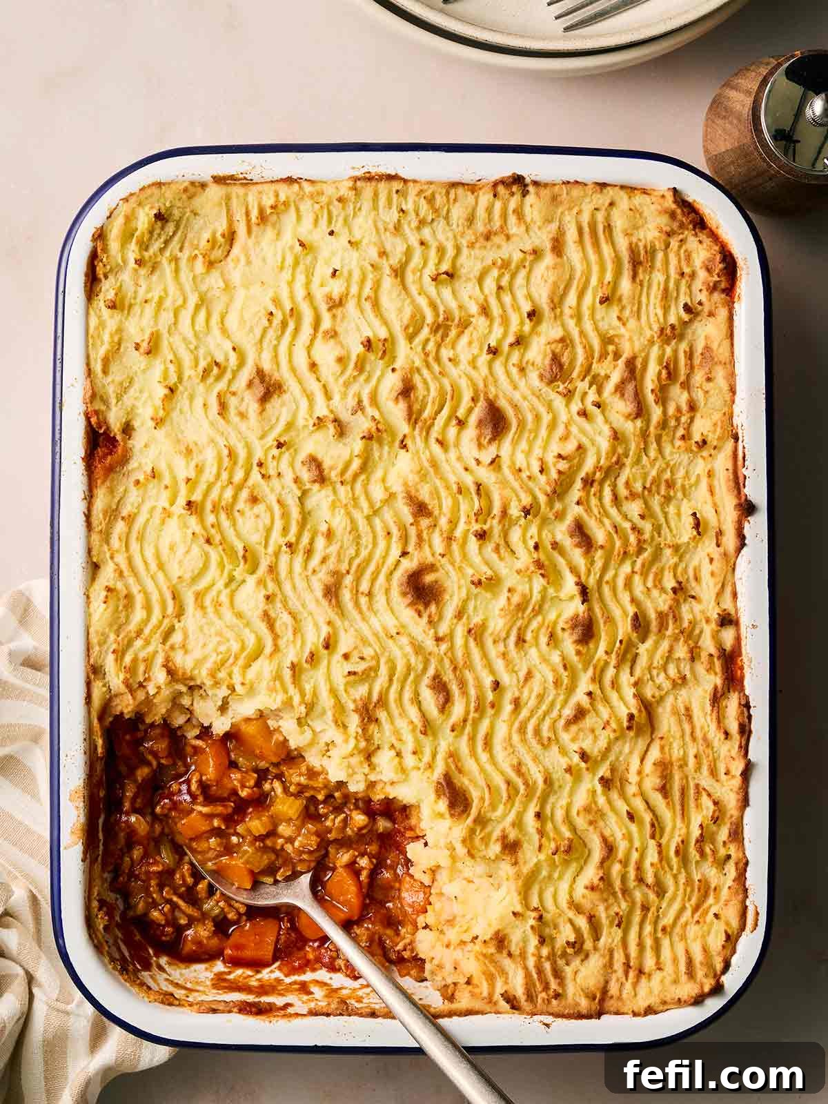 Homestyle Shepherd's Pie 2 A golden-topped shepherd's pie in a pan, with a portion missing and spoon serving.