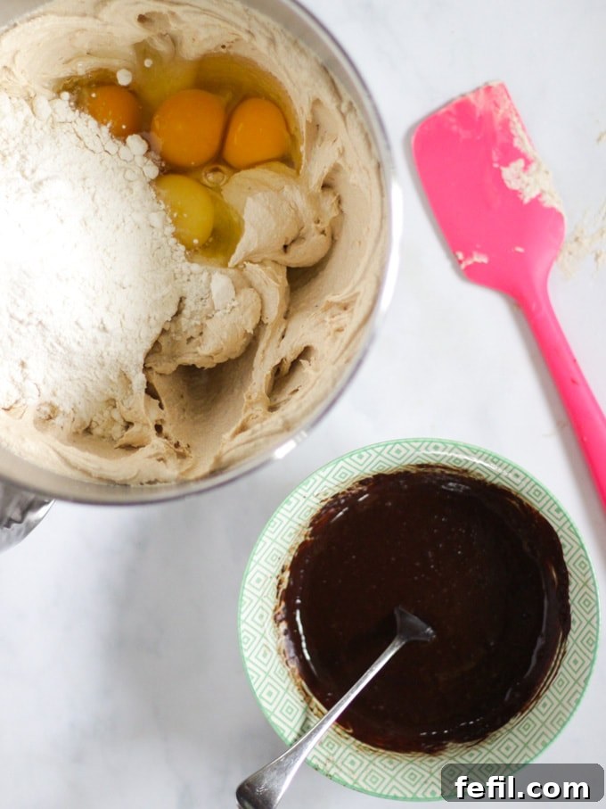Cake batter ingredients in a mixing bowl with a pink spatula, next to a bowl of cocoa and malt paste ready to be added.