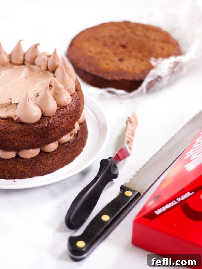 A chocolate cake layer being expertly piped with malt chocolate icing, ready for stacking.