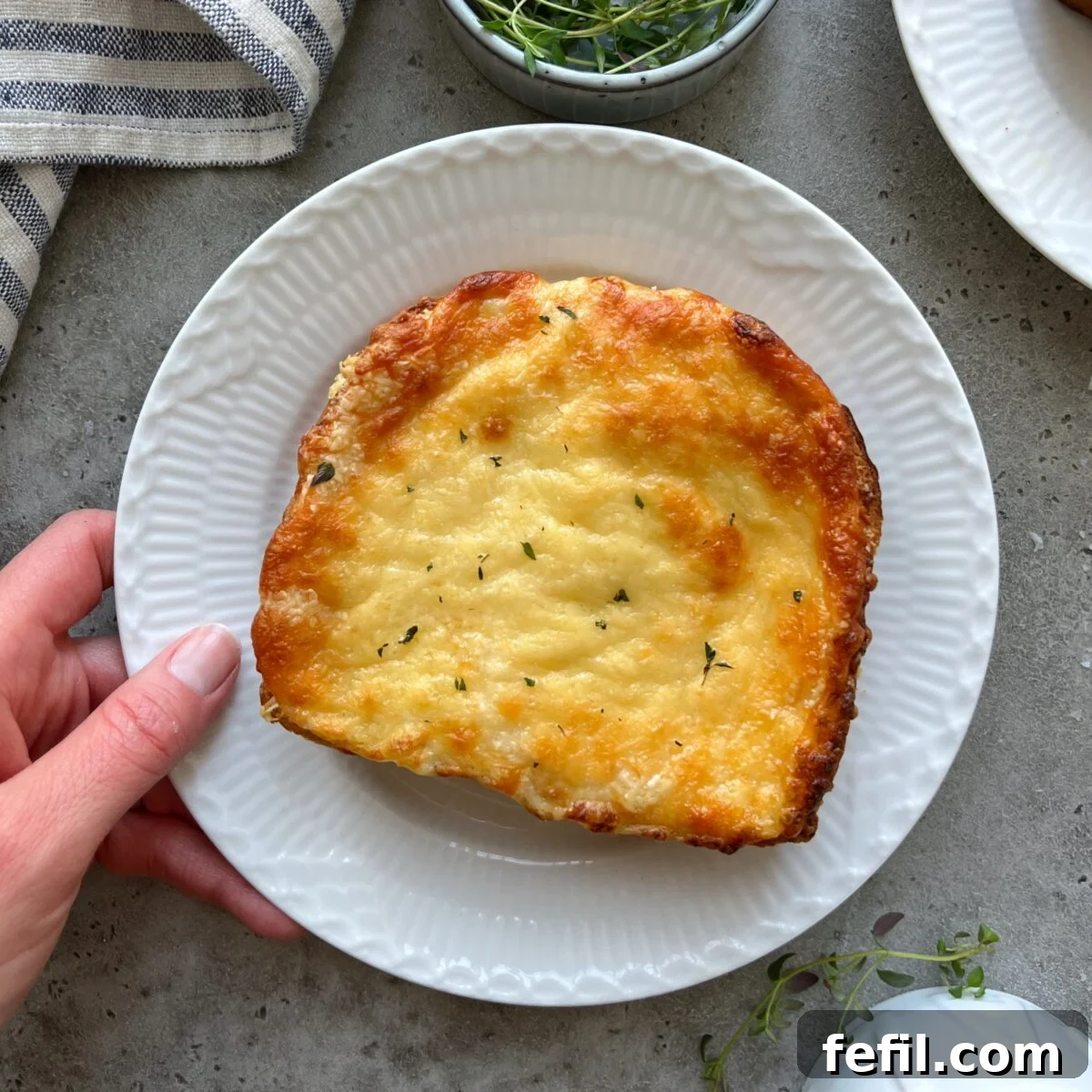Golden Baked Ham and Cheese Sandwich 4 A hand presents a pristine white plate featuring a perfectly baked, golden-brown Croque Monsieur, highlighting its inviting, cheesy exterior and elegant simplicity.
