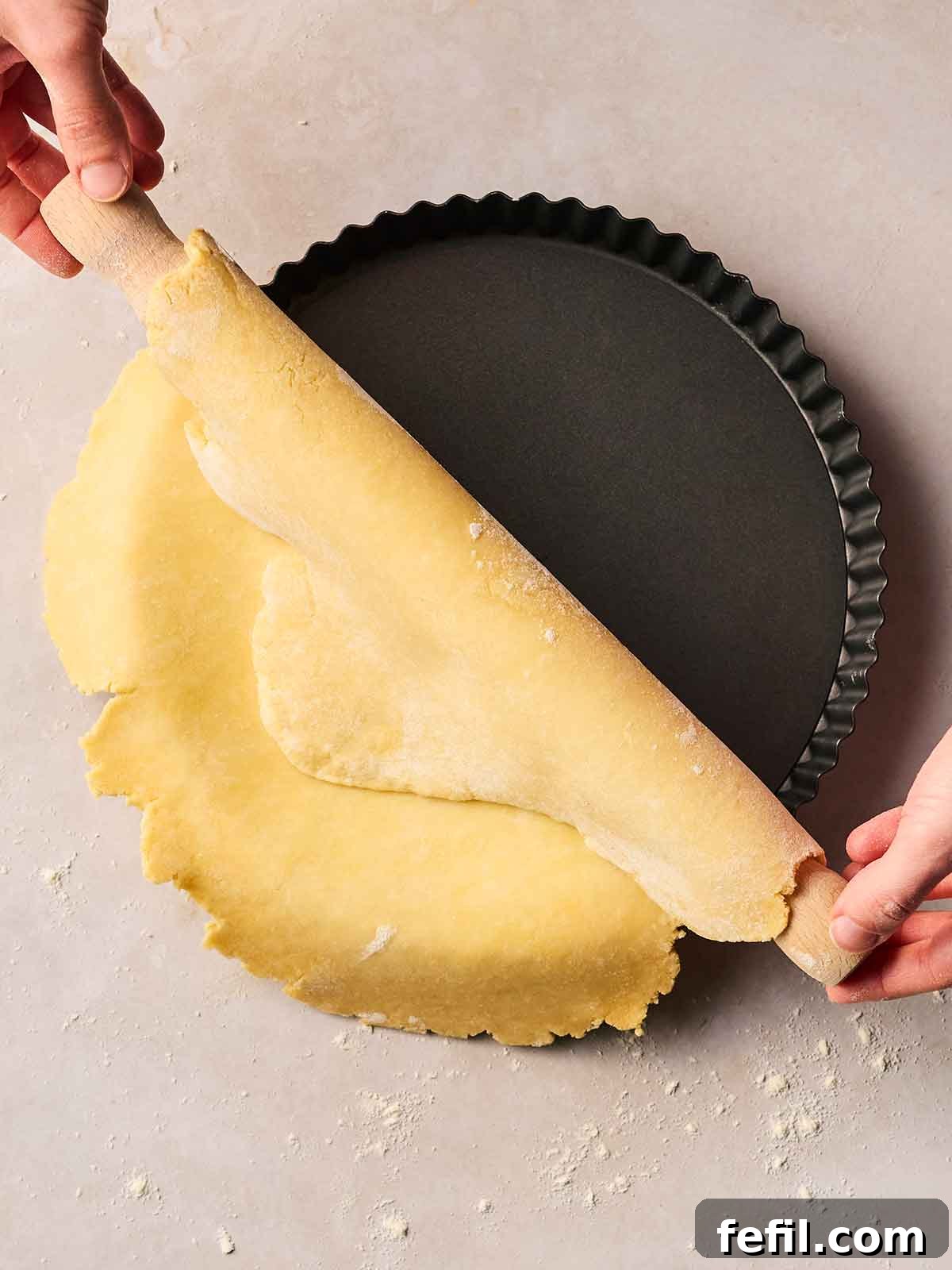 A flan dish with two hands rolling over homemade pie crust into it.
