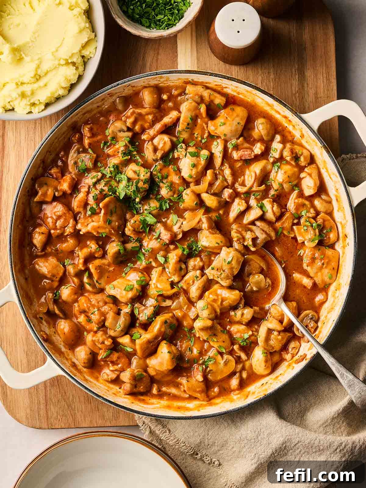 A large pot of golden-brown chicken chasseur simmering on a stove, ready to be served, accompanied by fluffy mashed potatoes and vibrant green beans in rustic bowls.