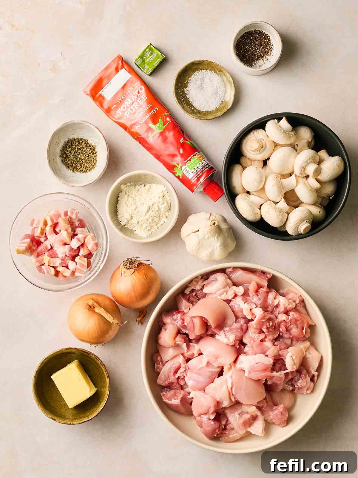 All the fresh ingredients meticulously laid out on a clean white countertop, ready to prepare Chicken Chasseur, including chicken thighs, mushrooms, onions, garlic, herbs, and bacon.