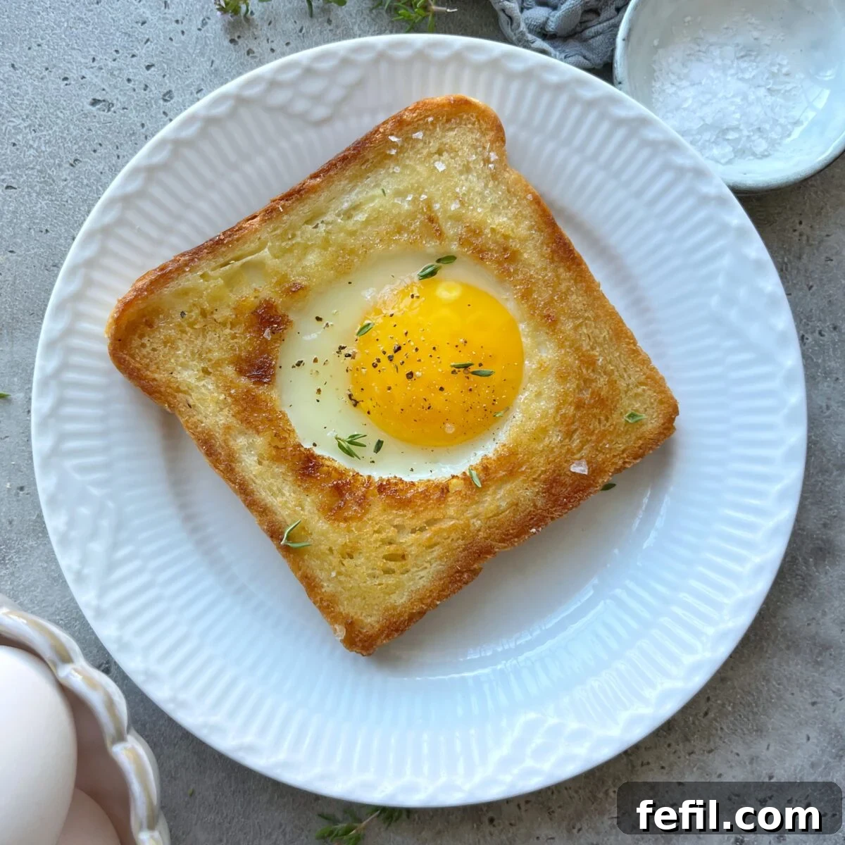 Egg-in-a-Hole Recipe: Crispy Toast with Runny Yolk 2 Toasted white bread filled with an egg in the center and topped with fresh thyme.