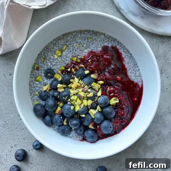Egg-in-a-Hole Recipe: Crispy Toast with Runny Yolk 11 A white bowl of chia pudding and Greek yogurt topped with fresh blueberries, berry compote, and chopped pistachios, placed on a gray surface.