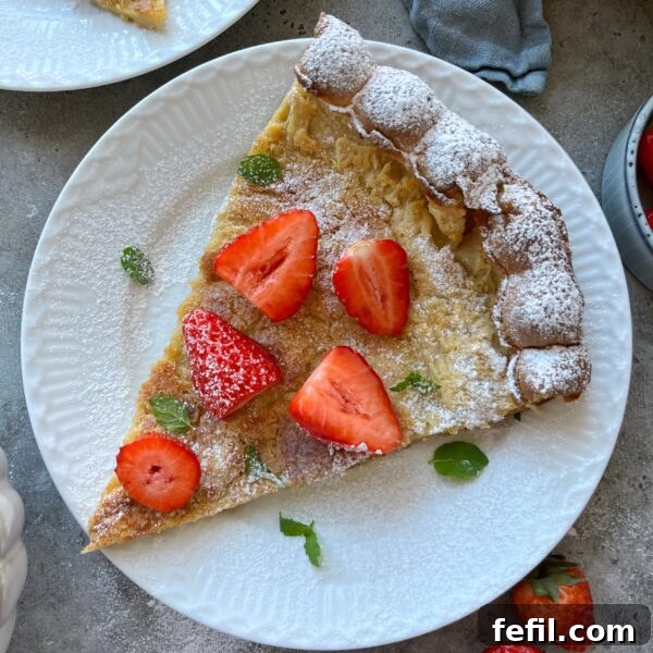 Egg-in-a-Hole Recipe: Crispy Toast with Runny Yolk 12 A slice of Dutch baby pancake topped with powdered sugar, fresh strawberry halves, and mint leaves rests on a white plate.
