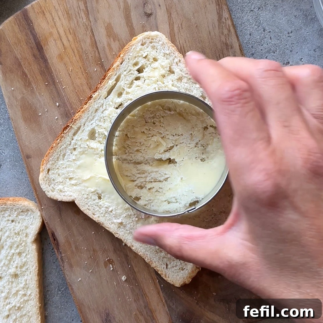 Egg-in-a-Hole Recipe: Crispy Toast with Runny Yolk 5 A hand uses a round cookie cutter to cut out a hole from a slice of buttered toast.