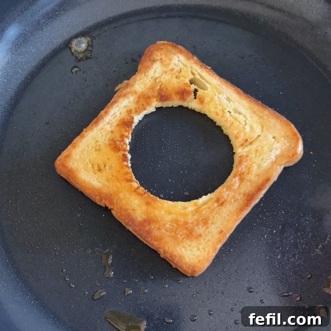 Egg-in-a-Hole Recipe: Crispy Toast with Runny Yolk 6 A piece of golden brown toast with a hole in it is frying in a pan.