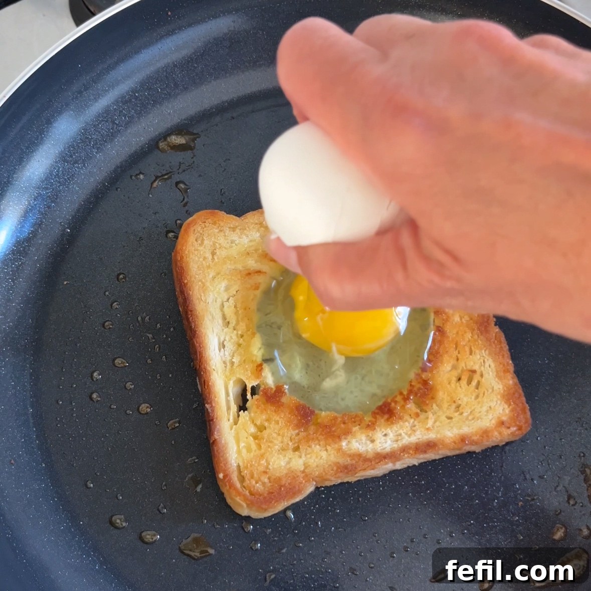 Egg-in-a-Hole Recipe: Crispy Toast with Runny Yolk 7 A hand cracks open an egg into a hole cut out from a piece of toast.