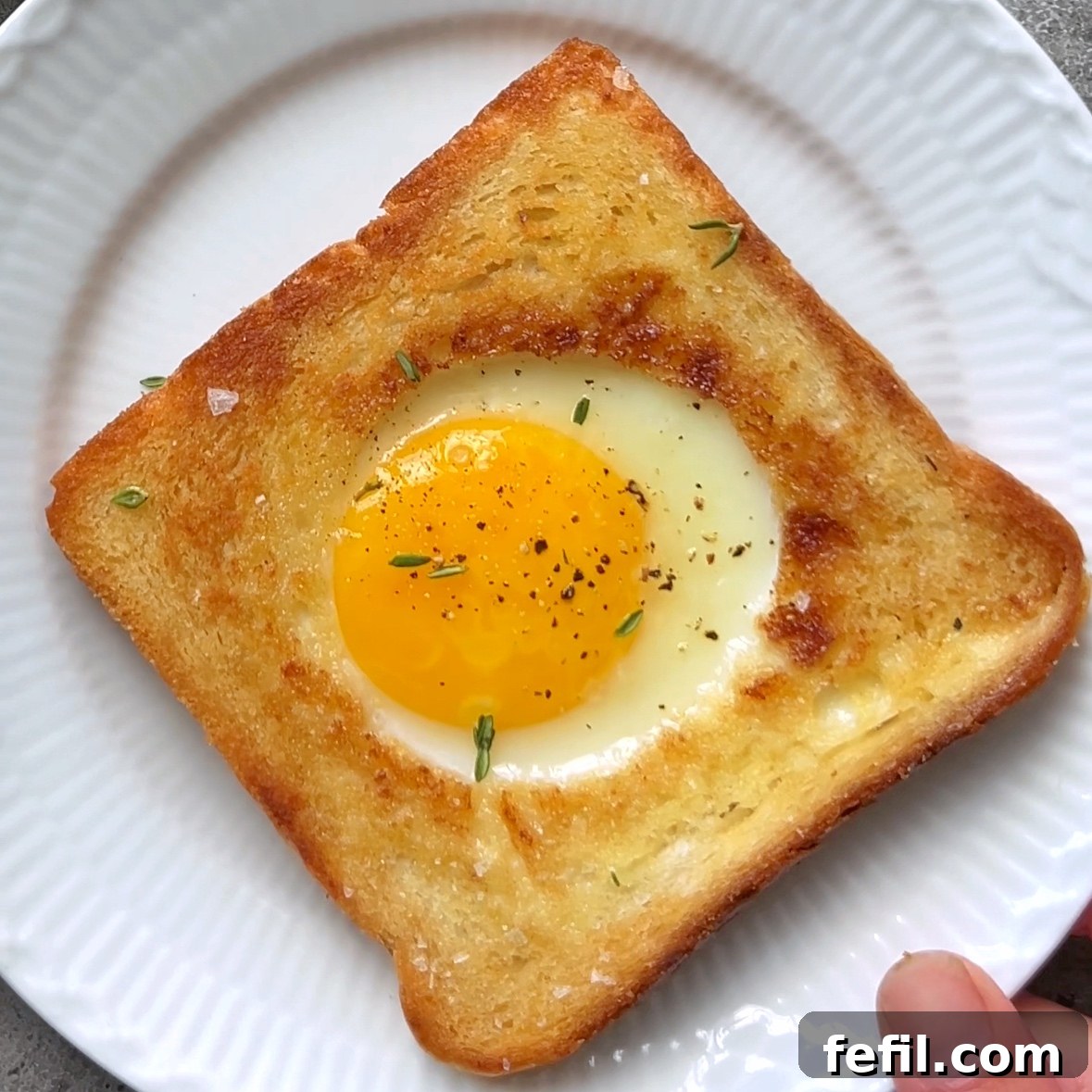 Egg-in-a-Hole Recipe: Crispy Toast with Runny Yolk 8 A white plate is topped with a freshly made golden-brown toast with a cooked egg in the center. The yolk is runny.