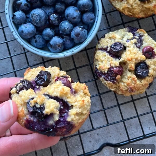 Egg-in-a-Hole Recipe: Crispy Toast with Runny Yolk 10 A hand holds a blueberry muffin next to a bowl of fresh blueberries and more muffins, all resting on a black wire cooling rack.