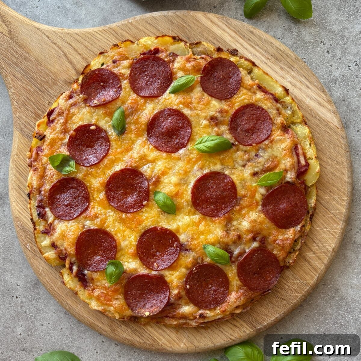Smashed potato pizza topped with basil on a chopping board.