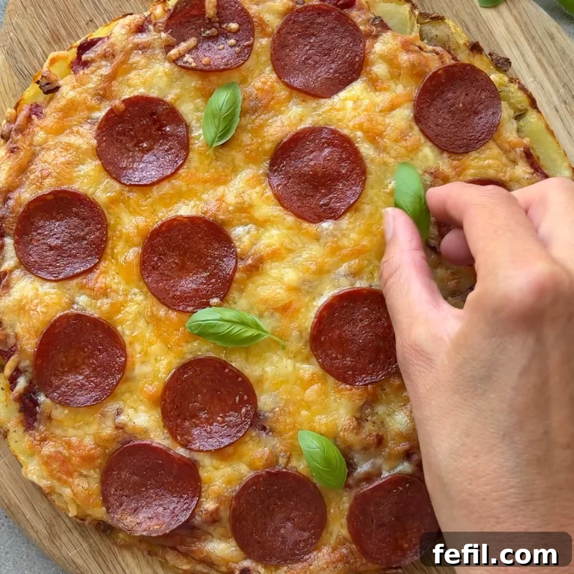 A hand places fresh basil onto a smashed potato pizza.