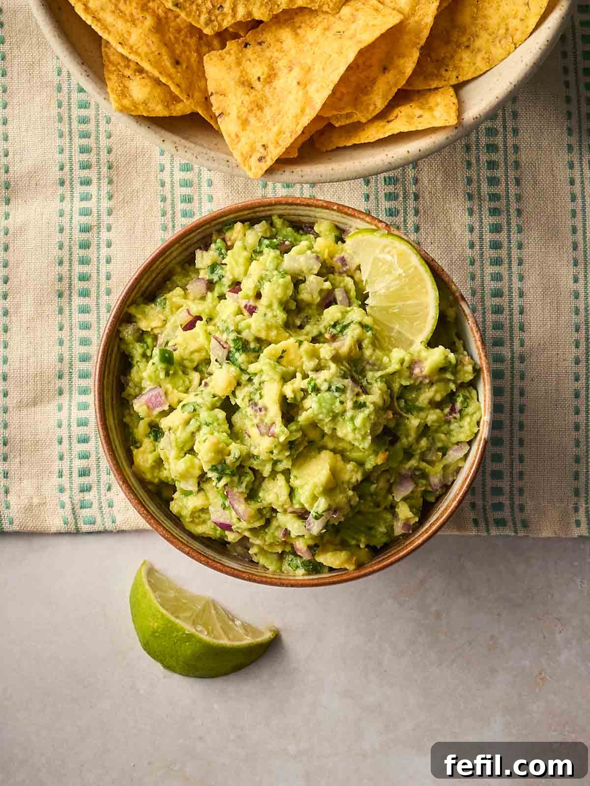 Fresh Guacamole Recipe: Zesty Homemade Mexican Dip 2 A bowl of homemade guacamole on a table with a tablecloth, and tortilla chips to the side and a wedge of lime.