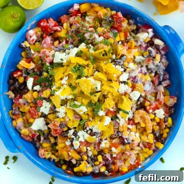 A big blue bowl filled with Mexican Salad, on a table surrounded with tortilla chips and limes.