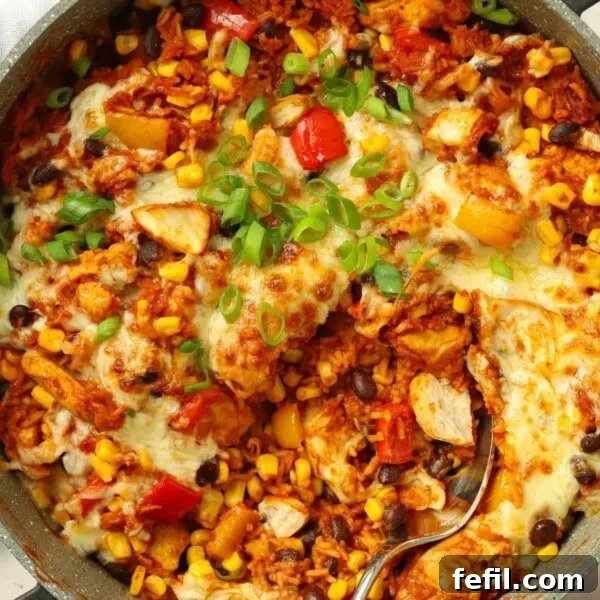 A round pan filled with chicken, rice, peppers, beans and topped with melted cheese for a Mexican chicken recipe.