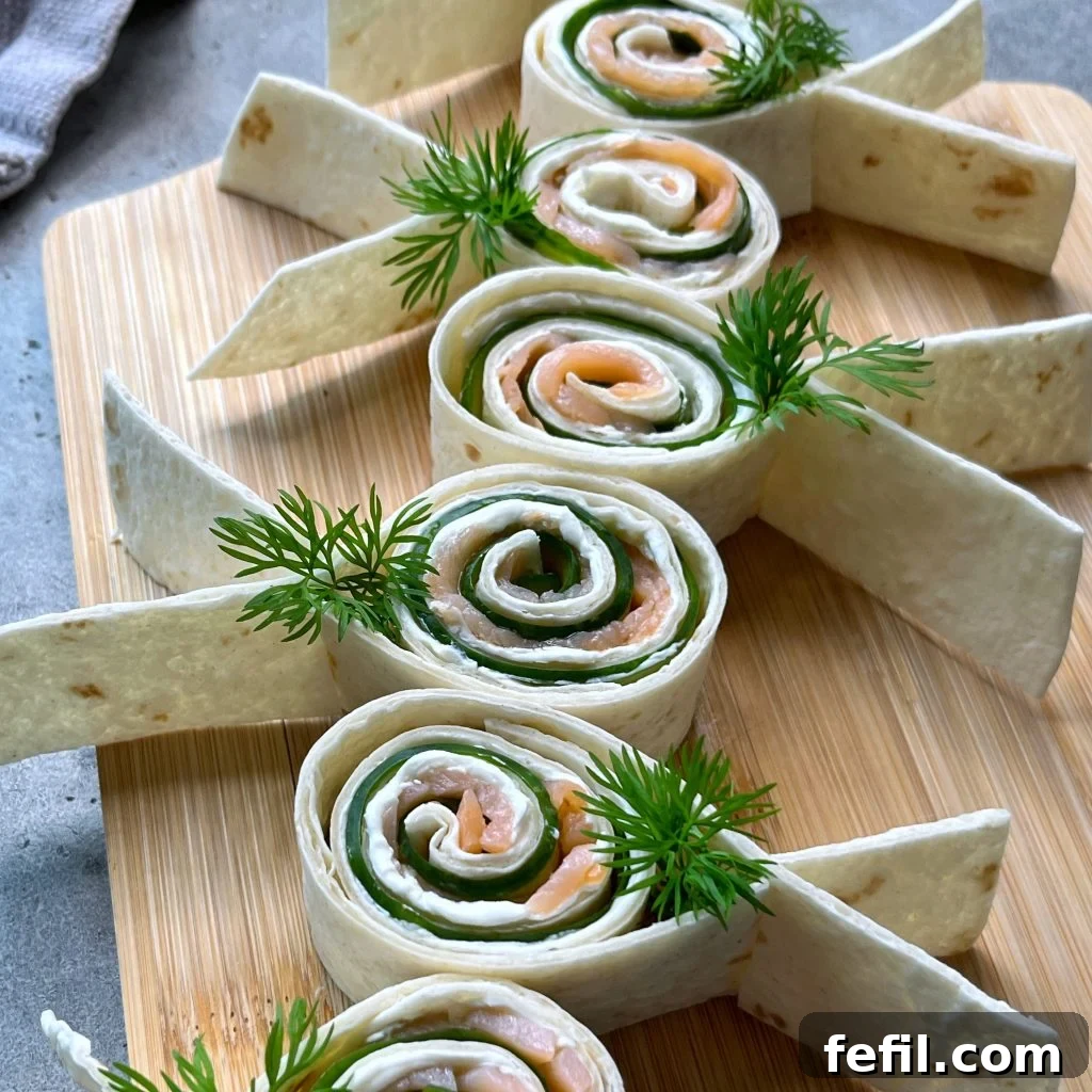 Smoked Salmon Pinwheels with Cream Cheese and Dill 2 Tortilla pinwheels filled with smoked salmon, cucumber, and cream cheese are arranged on a wooden board.