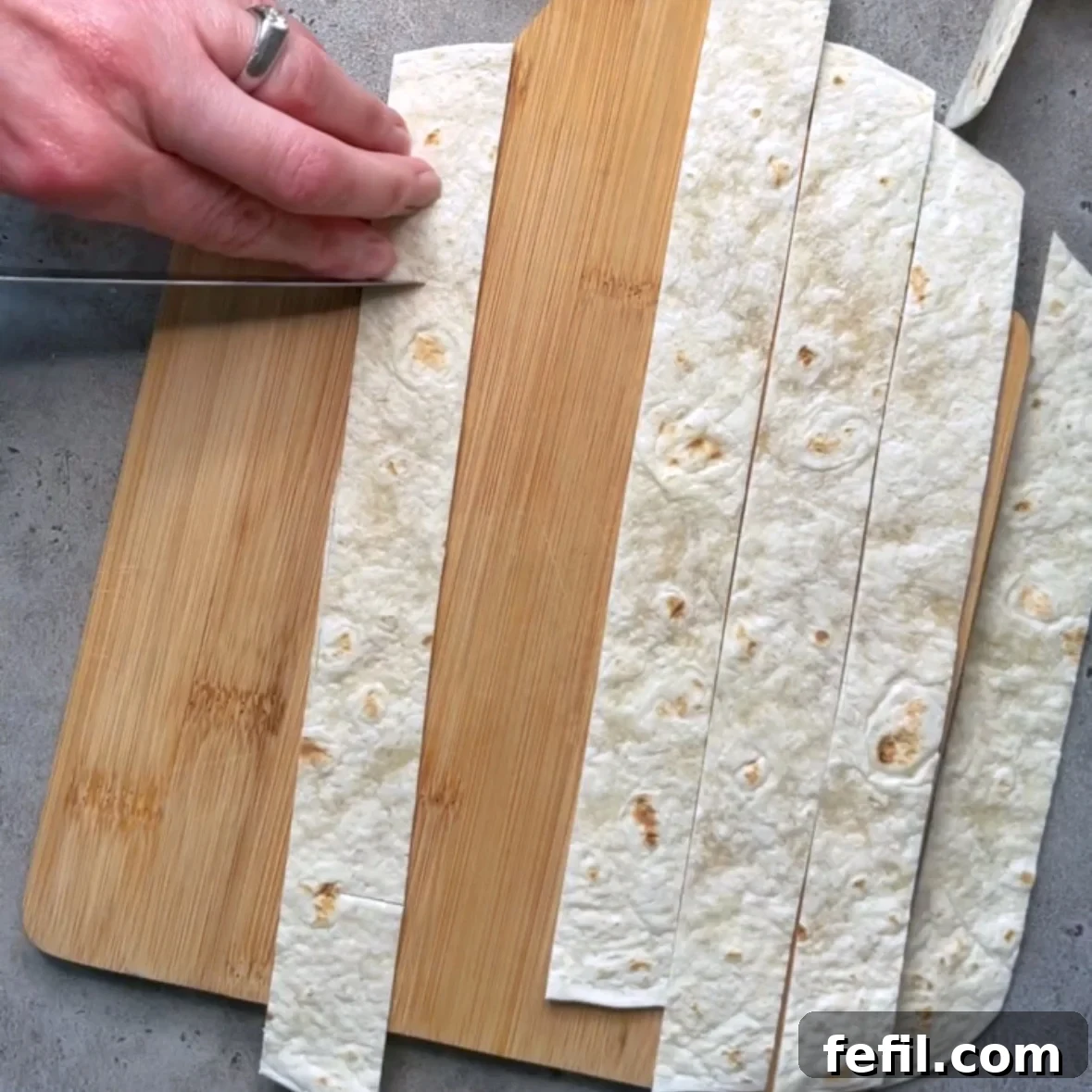 Smoked Salmon Pinwheels with Cream Cheese and Dill 3 A knife cuts an incision into a strip of tortilla to make tortilla ribbons.