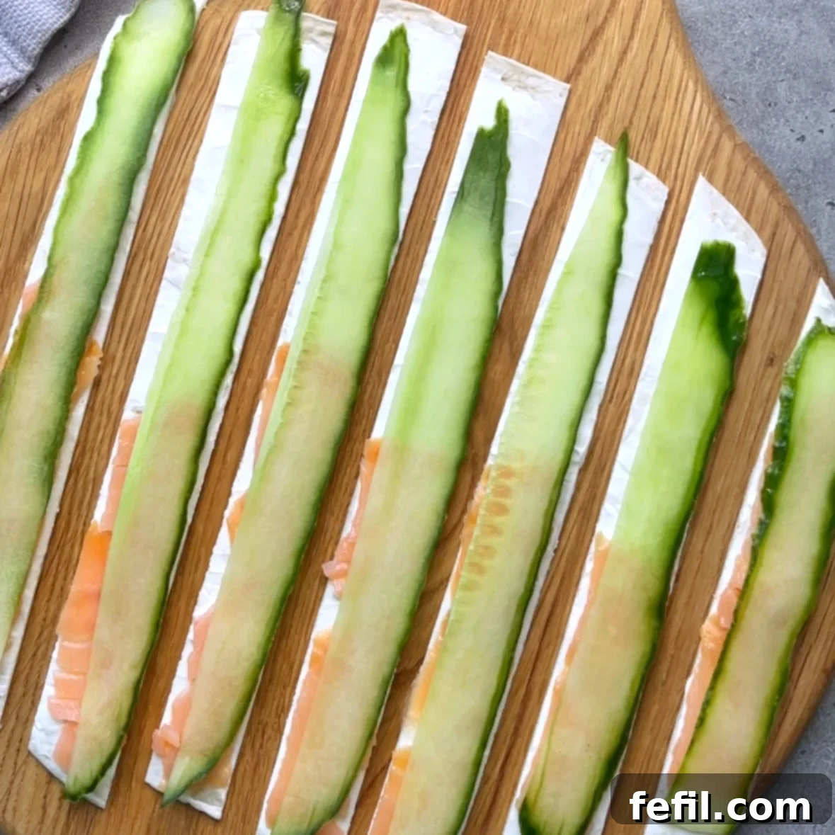 Smoked Salmon Pinwheels with Cream Cheese and Dill 5 Seven tortilla strips are topped with smoked salmon and cucumber and arranged on a wooden chopping board.