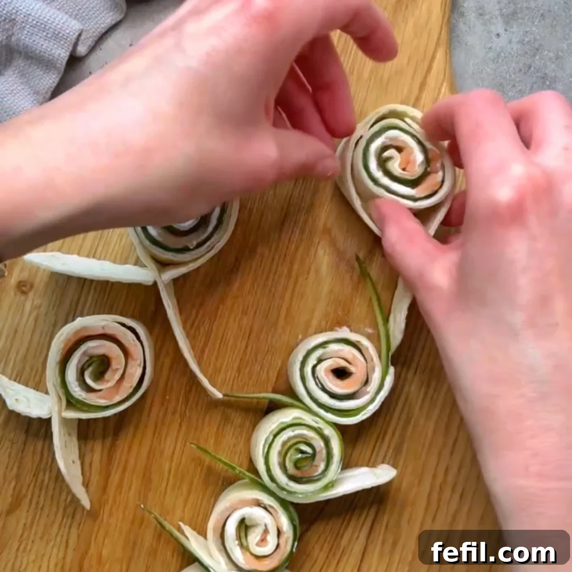 Smoked Salmon Pinwheels with Cream Cheese and Dill 6 A hand places a smoked salmon and cucumber roll up into a tortilla ribbon to hold them together.