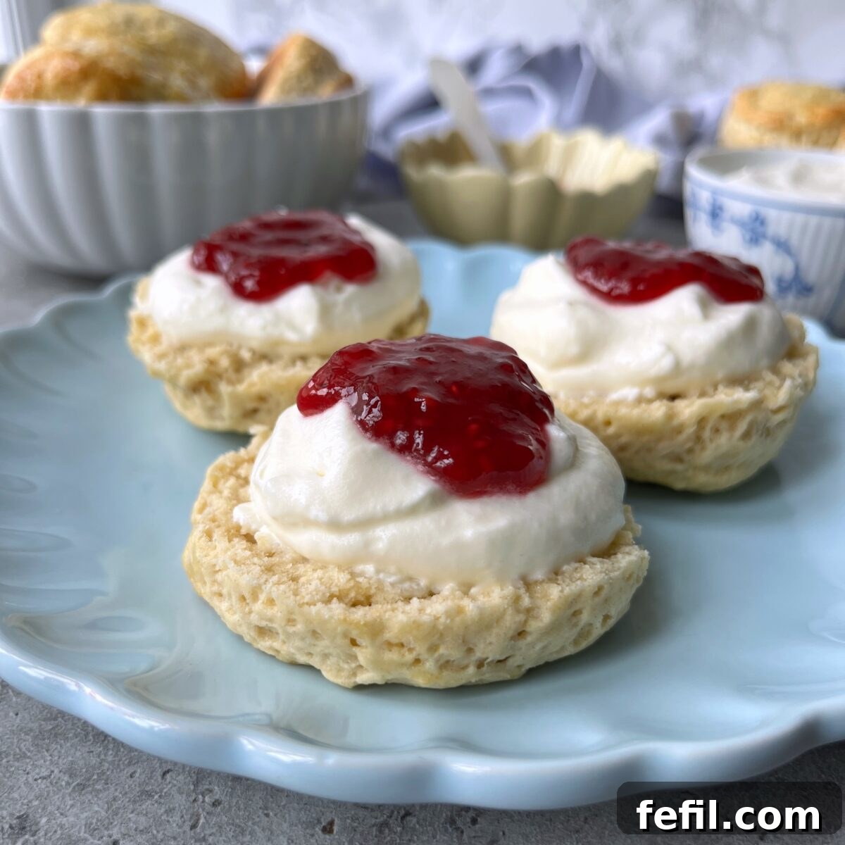Three scones topped with whipped cream and red jam sit on a light blue plate.