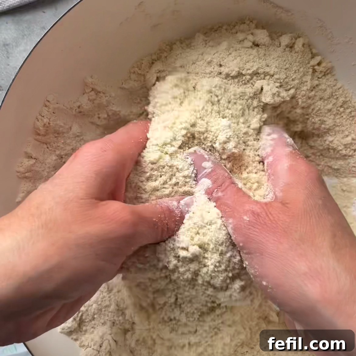 Two hands rub cold butter into a flour mixture.