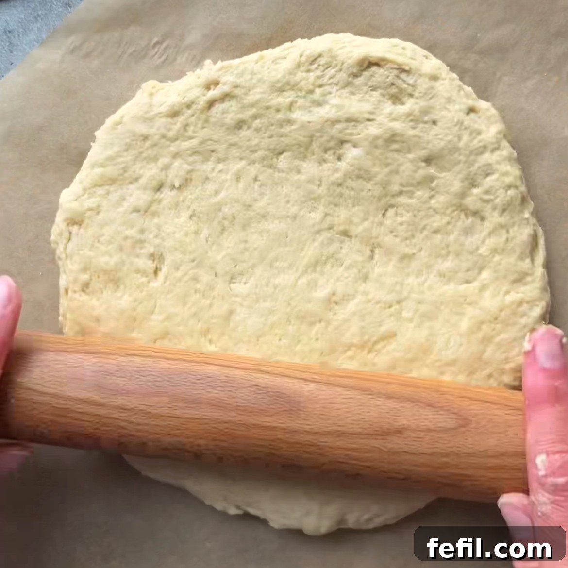 Two hands are rolling out dough with a wooden rolling pin.