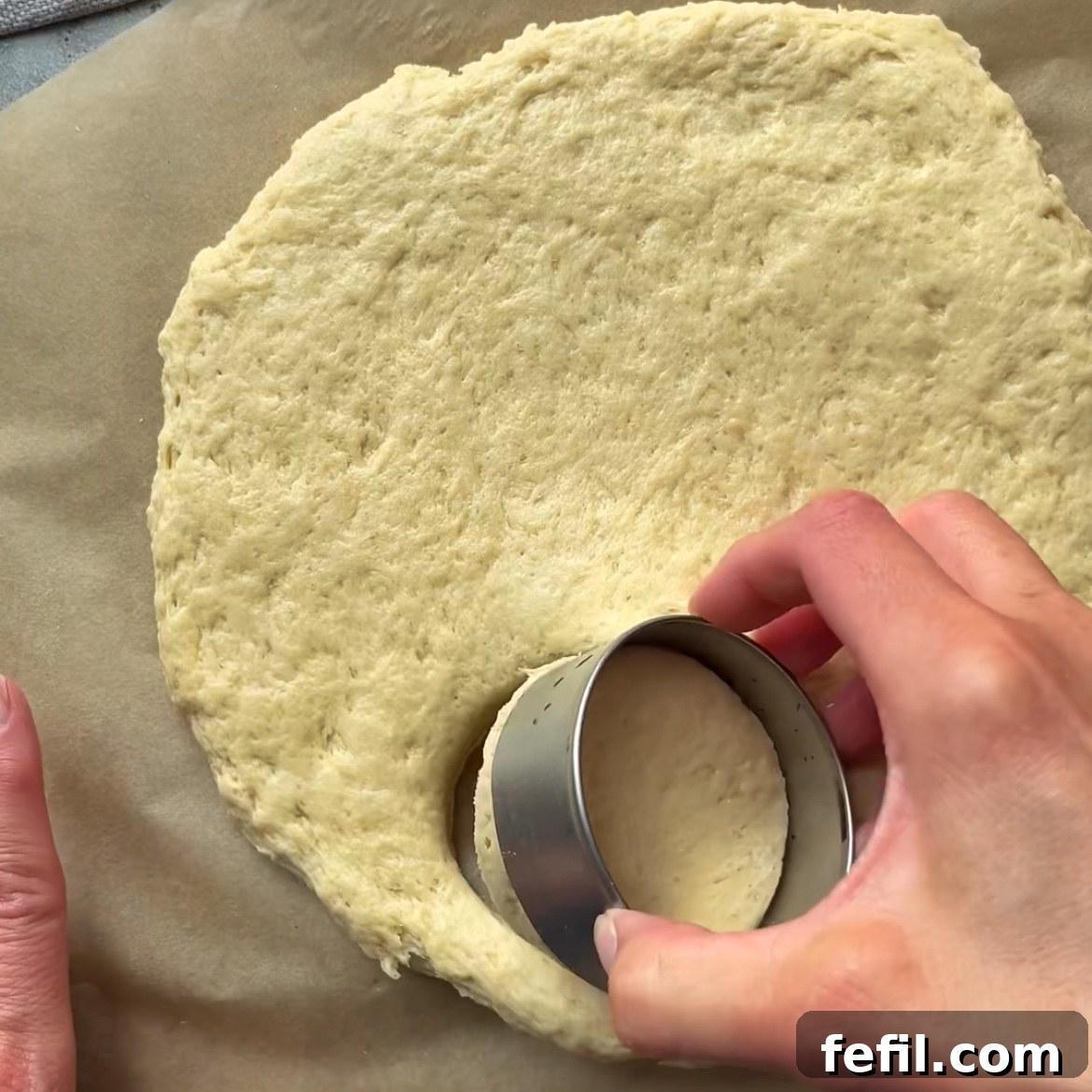 A hand is cutting out scones from a rolled out dough with a round cutter.