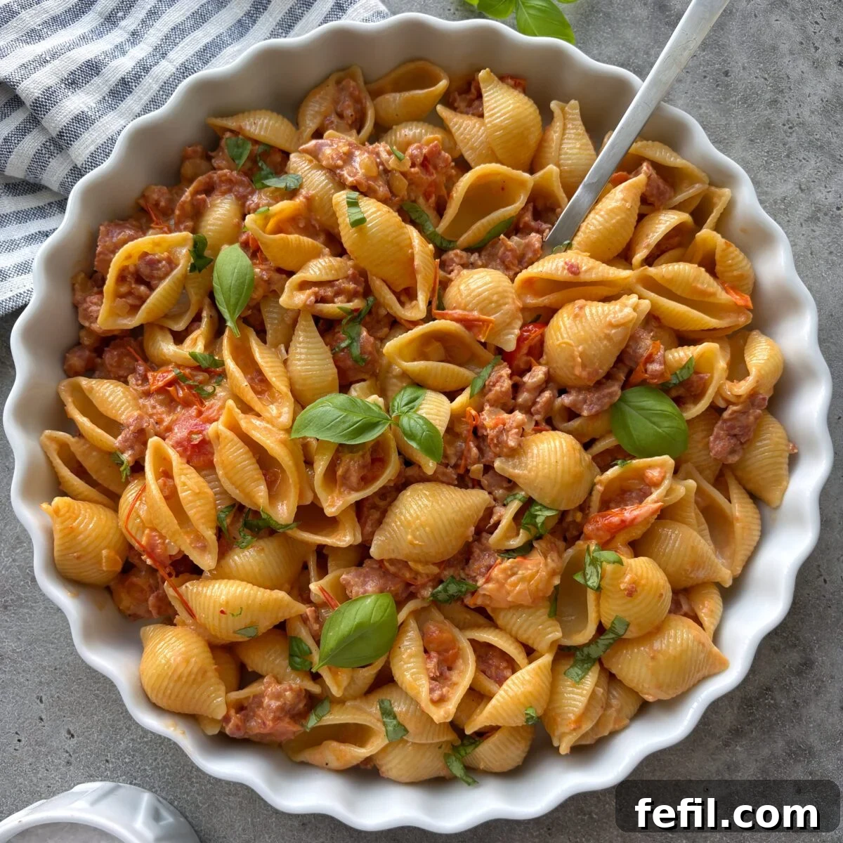 Spicy Italian Sausage Pasta Recipe 2 A bowl of freshly made Spicy Italian Sausage Pasta with a striped tea towel and fresh basil in the background.