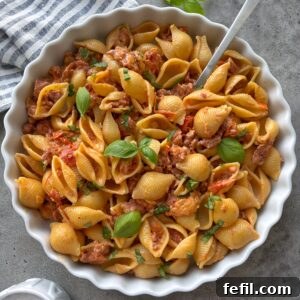 A bowl of freshly made Spicy Italian Sausage Pasta with a striped tea towel and fresh basil in the background.