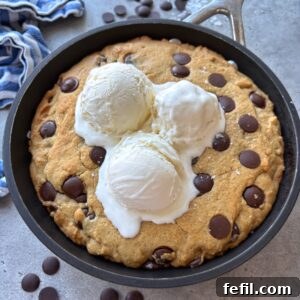 Gooey Chocolate Chip Skillet Cookie Recipe 10 Chocolate Chip skillet cookie topped with three scoops of vanilla ice cream. In the background are more chocolate chips and a blue striped tea towel.