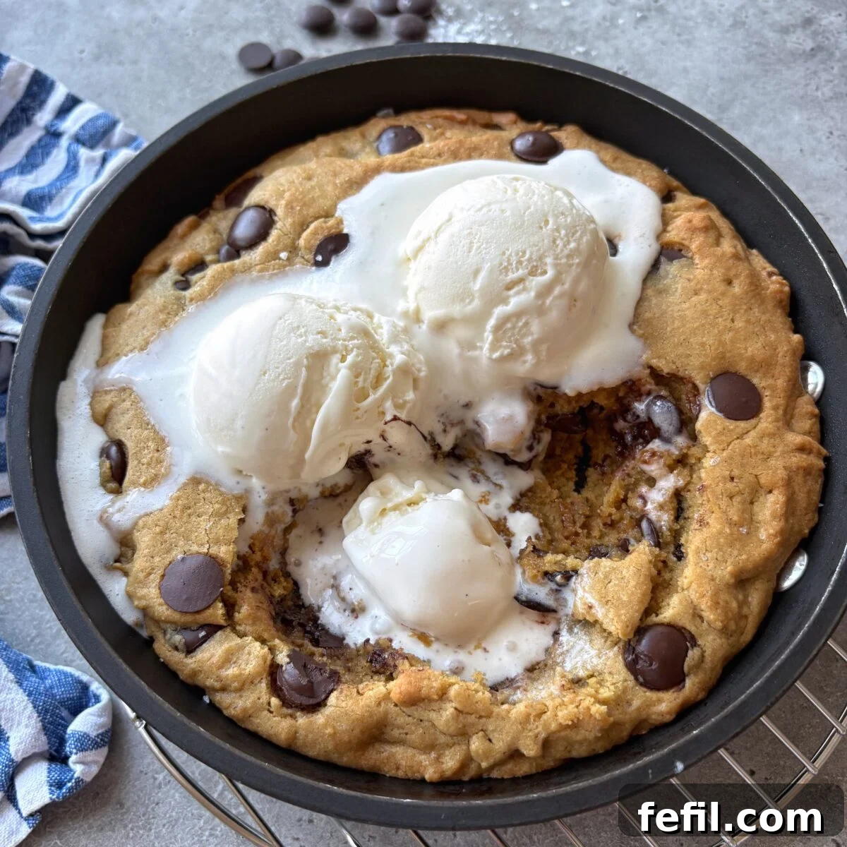 Gooey Chocolate Chip Skillet Cookie Recipe 4 A close up of a chocolate chip pizookie topped with vanilla ice cream with the center scooped out.