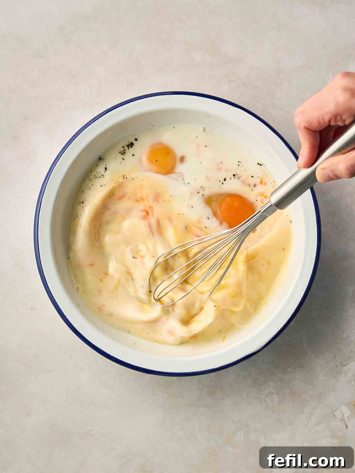 How to Make Classic Eggy Bread (British-Style French Toast) 6 A hand holding a whisk, whisking a mixture of eggs and milk in a wide bowl.