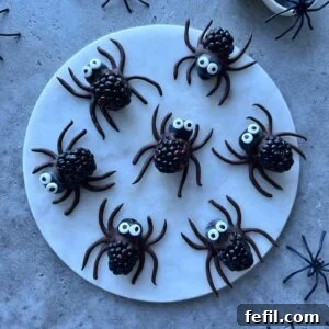 Halloween Chocolate Spider Treats for Parties 12 Seven spider-shaped treats made from blackberries, blueberries, chocolate, and candy eyes are arranged on a round white plate.