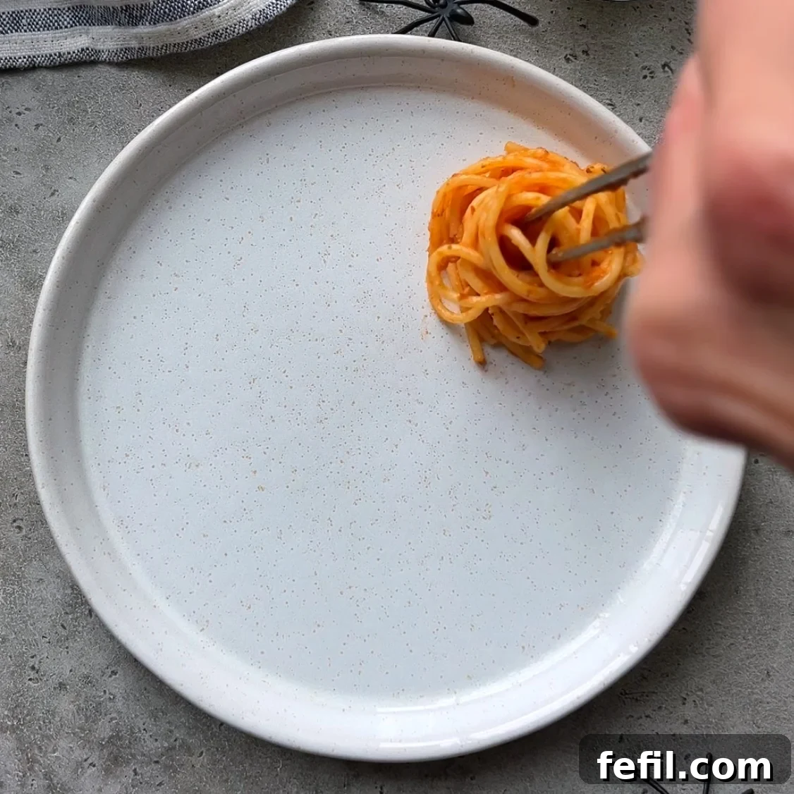 Spooky Halloween Spaghetti with Creepy Meatball Eyes 6 A hand uses food tweezers to arrange a tomato and spaghetti nest onto a serving platter.