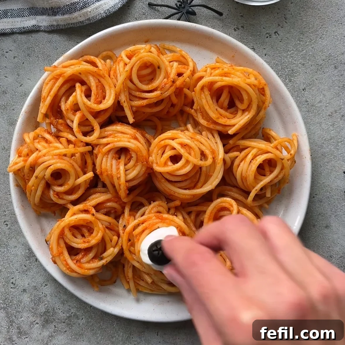 Spooky Halloween Spaghetti with Creepy Meatball Eyes 7 A hand tops tomato pasta nests with mozzarella and olive eyeballs.