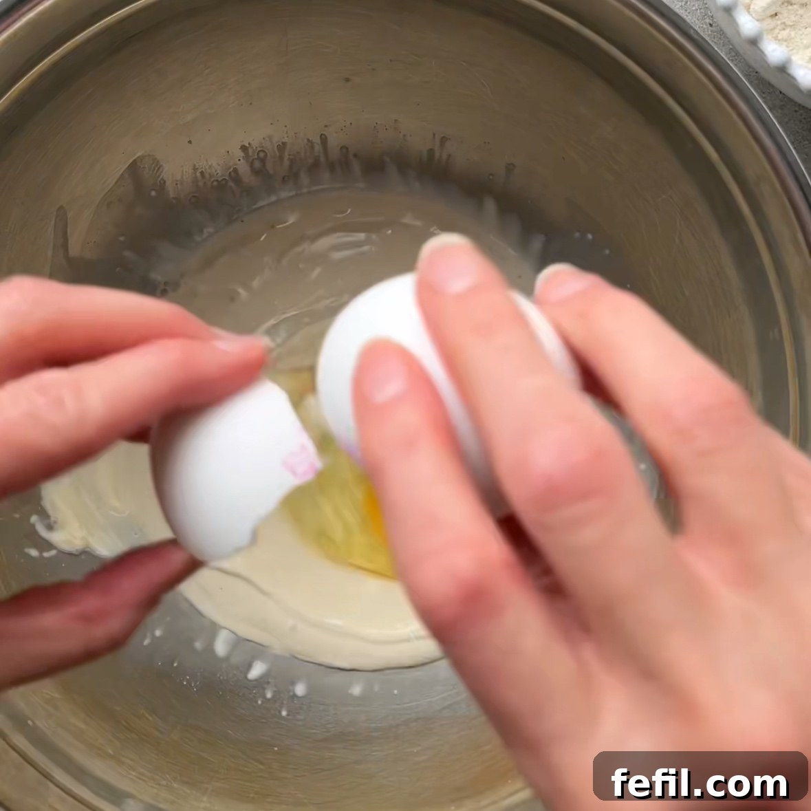 Mini Cinnamon Roll Bites with Cream Cheese Glaze 5 A person cracks an egg into a stainless steel bowl to make a mini cinnamon roll dough.