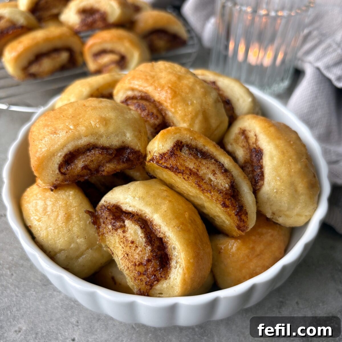 Mini Cinnamon Roll Bites with Cream Cheese Glaze 9 A sideview of mini cinnamon rolls in a bowl with more rolls in the background arranged on a cooling rack.